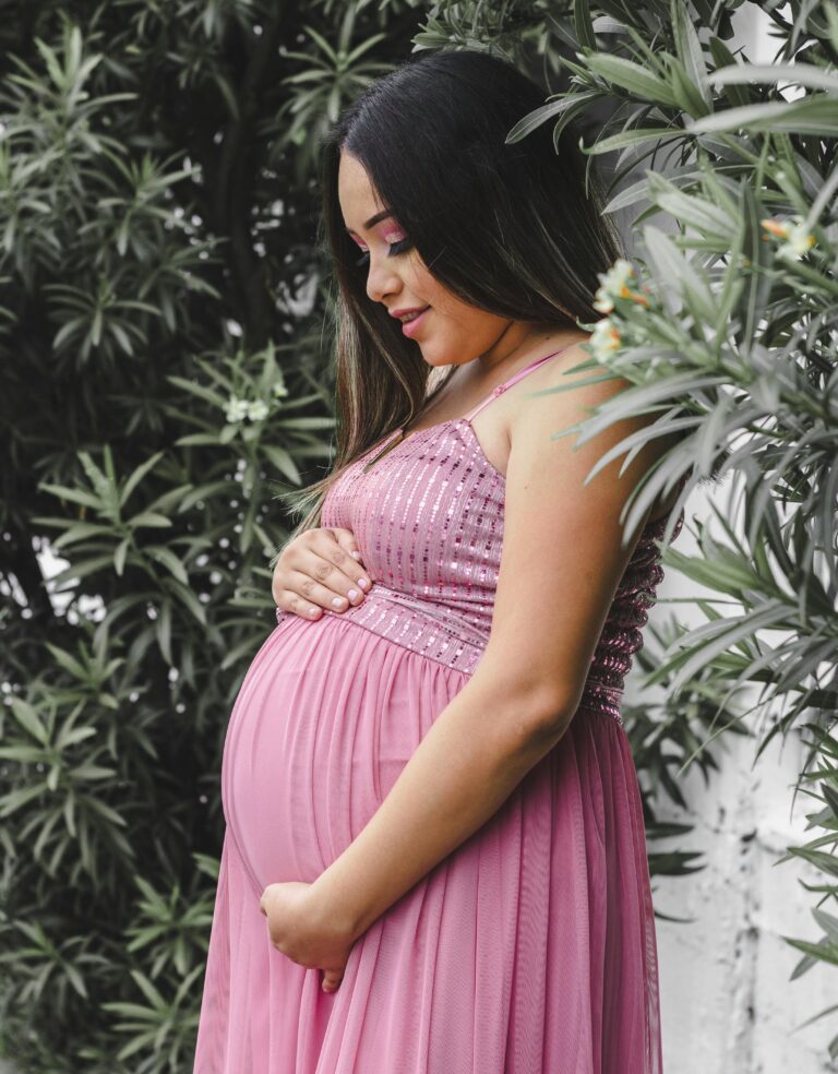 Pregnant woman in a pink dress standing in front of trees | Morning Sickness Remedies | Mary's Refuge | Martinsburg WV