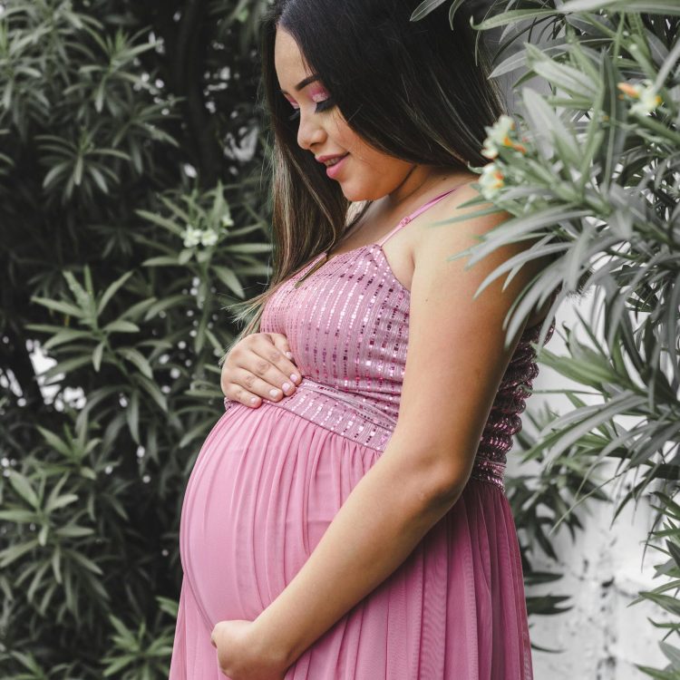 Pregnant woman in a pink dress standing in front of trees | Morning Sickness Remedies | Mary's Refuge | Martinsburg WV