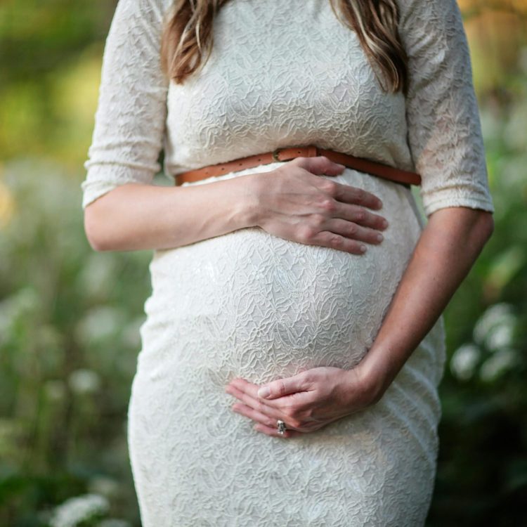 Pregnant women in a white dress holding her belly | Pregnancy symptoms | Mary's Refuge | Martinsburg WV