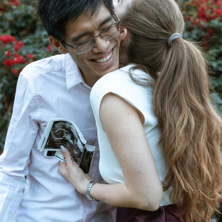 Man and woman embracing in a hug, the woman is holding an ultrasound of a baby | Unexpected Pregnancy Support | Mary's Refuge, Martinsburg WV