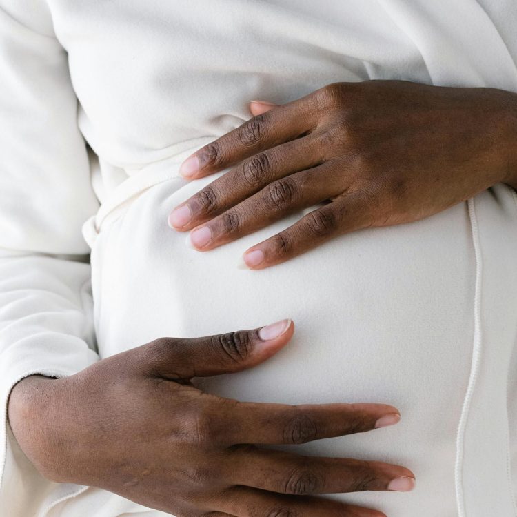 Black women holding her pregnancy belly in a white long sleeve shirt | Stories of Hope | Mary's Refuge | Martinsburg WV