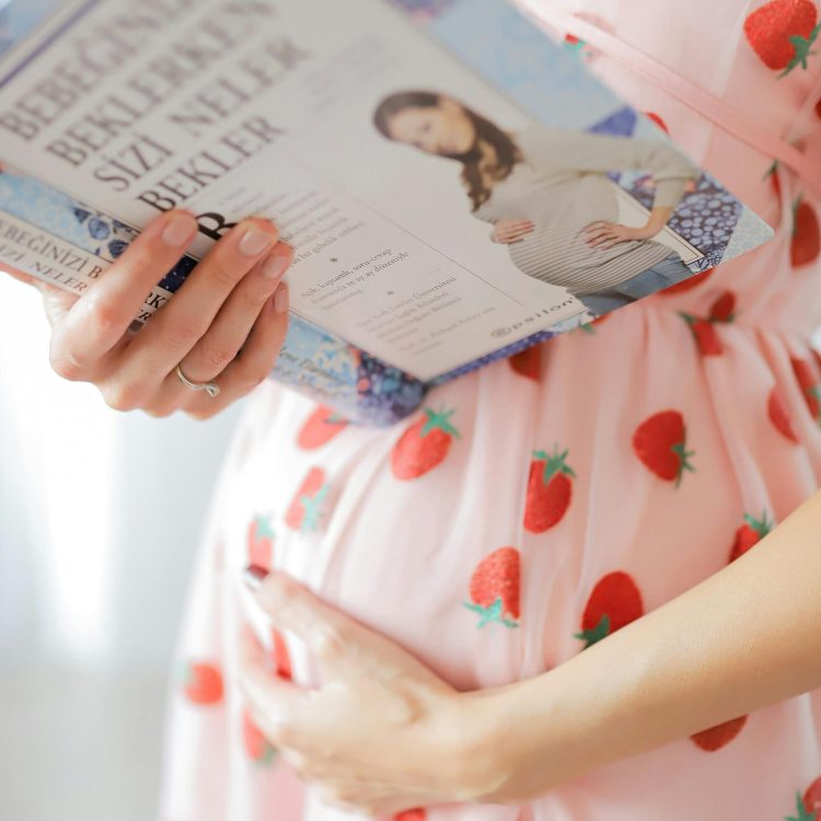 Pregnant women in a pink dress covered in strawberries reading a book about pregnancy | Determining the Due Date | Mary's Refuge | Martinsburg WV